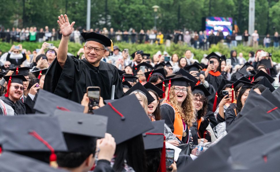 Man in graduation cap waves amongst crowd of graduates