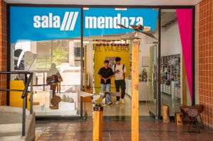 Entrance to Sala Mendoza with blue signage, glass doors and sculptural works positioned in the foreground.