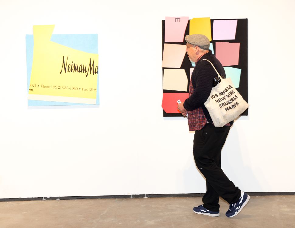 A fair visitor walks past two colorful abstract works on a white gallery wall.