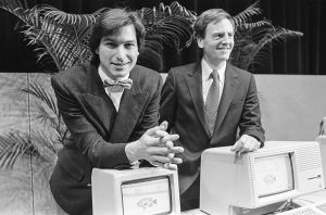 Two men in suits stand in front of desktop computers
