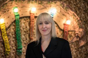 A blonde woman stands in front of an artwork