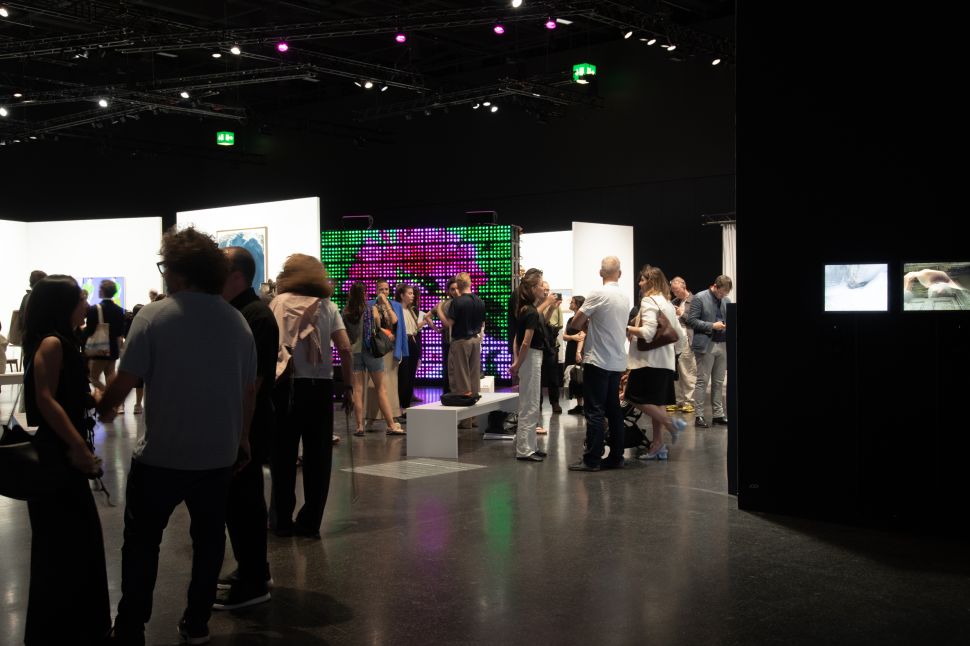 Visitors gather inside Art Basel’s Zero 10 section, where a large illuminated LED installation glows in green, pink and red.